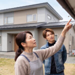 軒下にできた蜂の巣を確認する住人と作業員